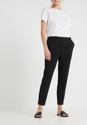 T-shirt en coton blanc associé à un pantalon noir à taille élastique avec poches latérales, jambes effilées, et sandales plates noires.