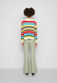 Monivärinen raidallinen neule, jossa vaihdellen leveitä raitoja; kermaiseva pohja, jossa punaisia, keltaisia, sinisiä ja mustia raitoja. Oliivinvihreät levenevät housut.