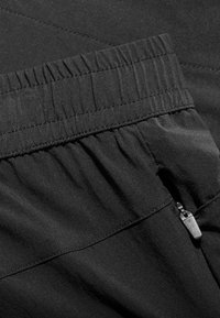 Black fabric with a gathered waistband feature, smooth texture, and a small zipper detail on the side for pocket access.