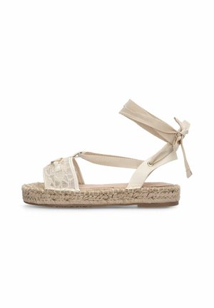 Sandale plate beige avec semelle en jute tissée, bride d'orteil à motif de dentelle et liens réglables en tissu autour de la cheville pour un maintien sûr.