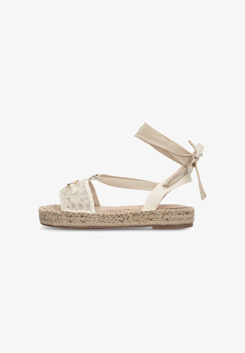 Beige flad sandal med flettet jutesål, snoremønster på tåremmen og justerbare stofremme omkring anklen for en sikker pasform.