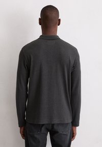 Ciemnoszara koszulka polo z długim rękawem i klasycznym kołnierzykiem, o gładkiej teksturze i luźnym kroju. Noszona z ciemnymi dżinsami, widok od tyłu.