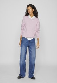 Light pink sweater with long sleeves, crew neck, layered over a white collared shirt, paired with wide-leg blue denim jeans and black shoes.