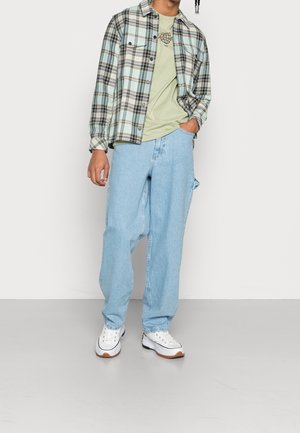 Plaid flannel shirt in light blue and black, paired with a light green t-shirt, baggy light blue jeans, and white sneakers.