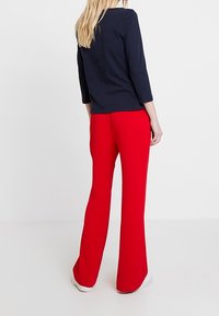 Námořnický dlouhý rukáv spojený s červenými rozšířenými kalhotami. Top má hladkou texturu; kalhoty jsou z pružného materiálu s upevněným pasem.