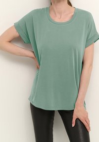 Mentolově zelené tričko s krátkým rukávem, kulatým výstřihem, hladkým povrchem a uvolněným střihem, kombinované s černými přiléhavými legínami.