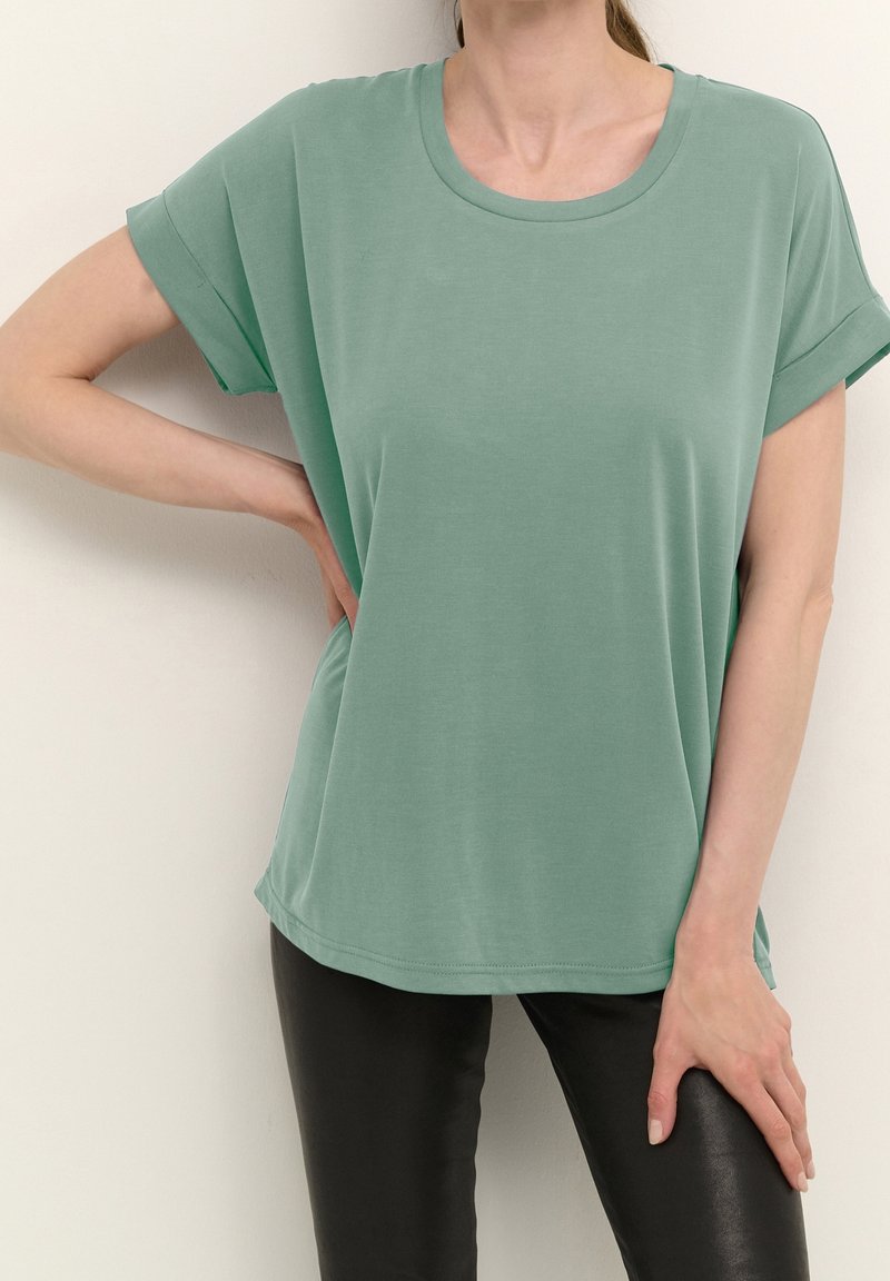 Mentolově zelené tričko s krátkým rukávem, kulatým výstřihem, hladkým povrchem a uvolněným střihem, kombinované s černými přiléhavými legínami.