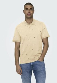 Polohemd aus hellgelbem Stoff mit kleinen schwarzen Blattmustern, einem klassischen Kragen, kurzen Ärmeln und einer lockeren Passform. Getragen mit blauen Jeans.