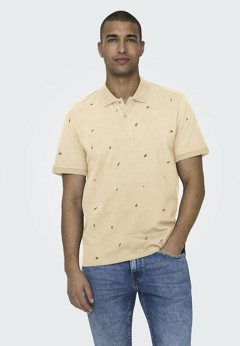 Polohemd aus hellgelbem Stoff mit kleinen schwarzen Blattmustern, einem klassischen Kragen, kurzen Ärmeln und einer lockeren Passform. Getragen mit blauen Jeans.