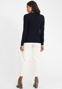 Navy-strickpullover mit strukturiertem Muster, enganliegenden Bündchen, kombiniert mit weißen weitem Hosen und gemusterten Stiefeletten.