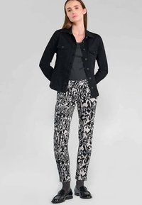 Zwarte denimjas, grijze top, zwart-witte patroonbroek en zwarte loafers. Gestructureerde stof met knoopdetails op de jas.