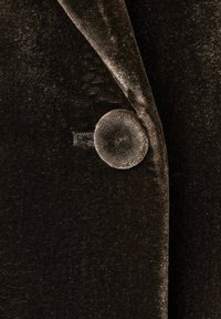 Detalle de un blazer de terciopelo negro que muestra un botón redondeado con una superficie texturizada, situado sobre un fondo de tela suave.