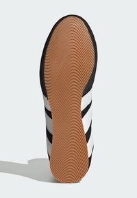 Czarno-biały sneaker z trzema czarnymi paskami, cholewka z teksturowanej tkaniny oraz gumowa podeszwa z falistym wzorem w kolorze beżowym.