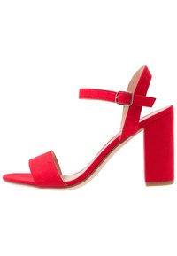 Red suede high-heeled sandal with a wide front strap, adjustable ankle strap, and a chunky block heel. Smooth inner lining complements the design.