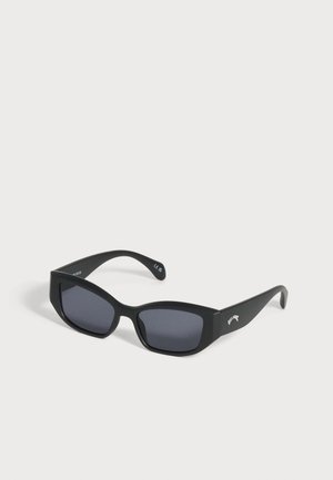 Lunettes de soleil rectangulaires noires avec verres foncés et montures épaisses, inclinées vers la droite sur fond blanc.