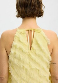 Yellow sleeveless top with layered fringed texture, featuring a keyhole back and a tie closure at the neck. Soft, flowing fabric.