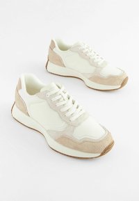 Zapatillas blancas con acentos de ante beige, con una puntera redondeada, cordones y una suela de goma texturizada para agarre.