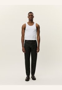 Hvit tank topp, mørk denim jeans og brune støvler. Modellen står rett opp mot en nøytral bakgrunn. Jeansene har klassisk passform.