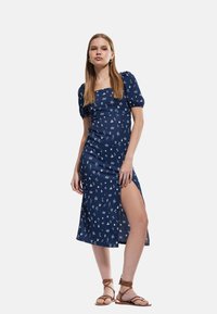 Vestido azul marino con mangas cortas abullonadas, escote cuadrado, patrón floral y abertura hasta el muslo. Fabricado con una tela texturada.
