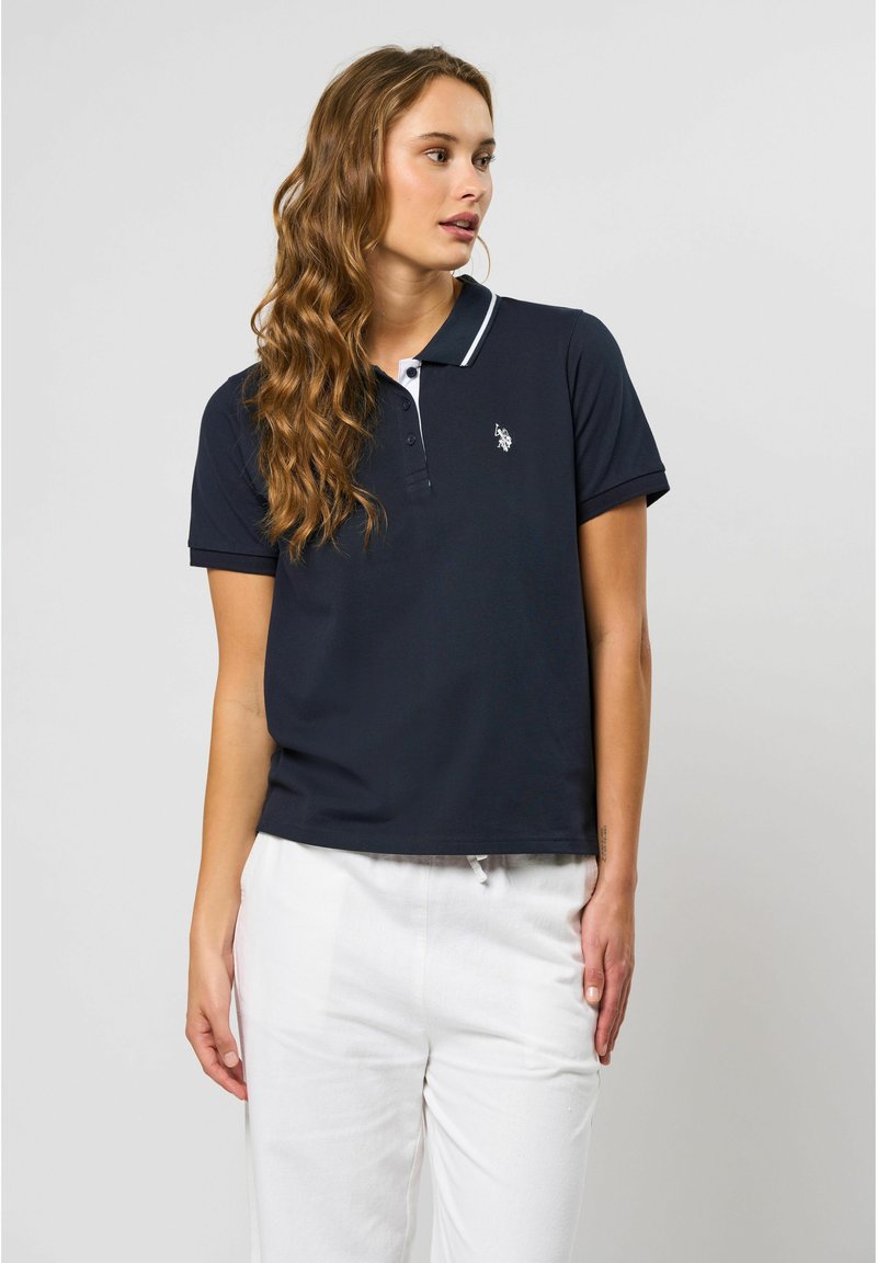 Mørkeblå polo med en hvid kantkrave og broderet logo. Korte ærmer, afslappet pasform, glat tekstur og ensfarvet design.