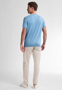 Pulover tricotat cu mânecă scurtă de culoare albastru deschis, cu un finisaj texturat, asociat cu pantaloni din in bej deschis și tenisi albi cu accente maronii.