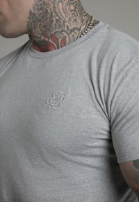 Grijze T-shirt met korte mouwen van een zachte stof, met een subtiele geborduurde logo op de borst. Gemiddelde pasvorm met een ronde halslijn.