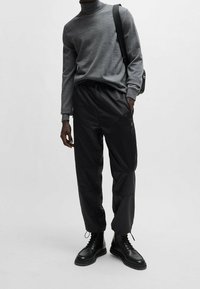 Grauer Rollkragenpullover, slim fit; schwarze Hose mit elastischem Bund und Taschen; schwarze Schnürstiefel; minimalistisches Design auf einfarbigem Hintergrund.