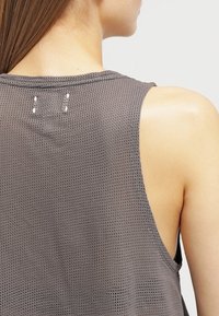 Top sin mangas de malla gris con un diseño sin mangas, pequeñas decoraciones cerca del escote y un acabado suave y texturizado.