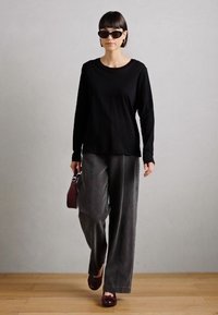 Chemise noire à manches longues associée à un pantalon large gris foncé. Les accessoires comprennent des lunettes de soleil noires et un sac à main bordeaux. Chaussures plates bordeaux.