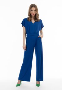 Royalblå jumpsuit med korte lette ærmer, V-hals og indsnævret talje; har sidelommer og svajede, brede bukser.