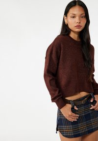 Brązowy sweter dzianinowy o skróconym kroju, z długimi rękawami i prążkowanym wykończeniem, zestawiony z niebieską mini spódnicą w kratę z bocznym rozcięciem.