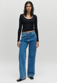 Schwarzes, langärmeliges, geripptes Oberteil, kombiniert mit hoch geschnittenen, lockeren blauen Jeans. Die Jeans verfügen über ein klassisches Fünf-Taschen-Design und Nähdetails.