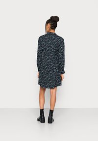 Vestido preto com padrão floral, apresentando mangas longas, cintura ajustada e uma saia fluida, combinado com botas pretas de tornozelo e vista traseira.