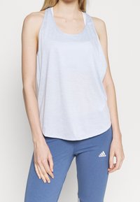 Top deportivo de color azul claro, hecho de una tela transpirable, con un dobladillo redondeado y un corte relajado, combinado con leggings azules.