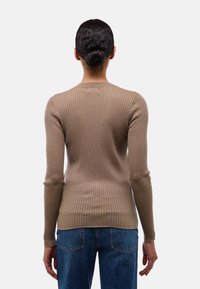 T-shirt à manches longues côtelé en marron clair, avec un col rond, une coupe ajustée et une texture douce. Accompagné d'un jean en denim bleu.