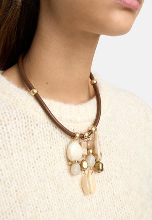 Brązowy naszyjnik ze skóry na sznurku z złotymi koralikami i kremowymi kamiennymi wisiorkami, noszony na białym dzianym swetrze na szyi osoby.