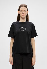 Zwarte katoenen t-shirt met korte mouwen, ronde hals en een witte grafische logo op de borst. Relaxte pasvorm, zachte textuur.