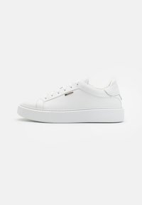 Zapatillas de cuero blancas con superficie texturizada, puntera redonda, suela de goma plana y talón reforzado, con un diseño minimalista y un detalle plateado.