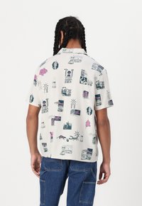 Short-sleeve shirt in light fabric, featuring a repeated graphic pattern with colorful prints on a white background. Relaxed fit.