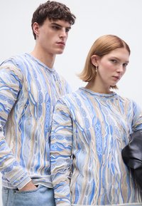 Ελαφρύ πλεκτό πουλόβερ με μοτίβο κυμάτων σε αποχρώσεις του μπλε, μπεζ και λευκού. Λαιμόκοψη με στρογγυλή γραμμή και ριμπ μανσέτες, με υφή που προσδίδει ιδιαίτερη όψη.