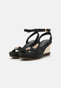 Black wedge sandals with fabric straps, ankle buckle, and decorative metal accent. Textured espadrille wedge and smooth footbed.
