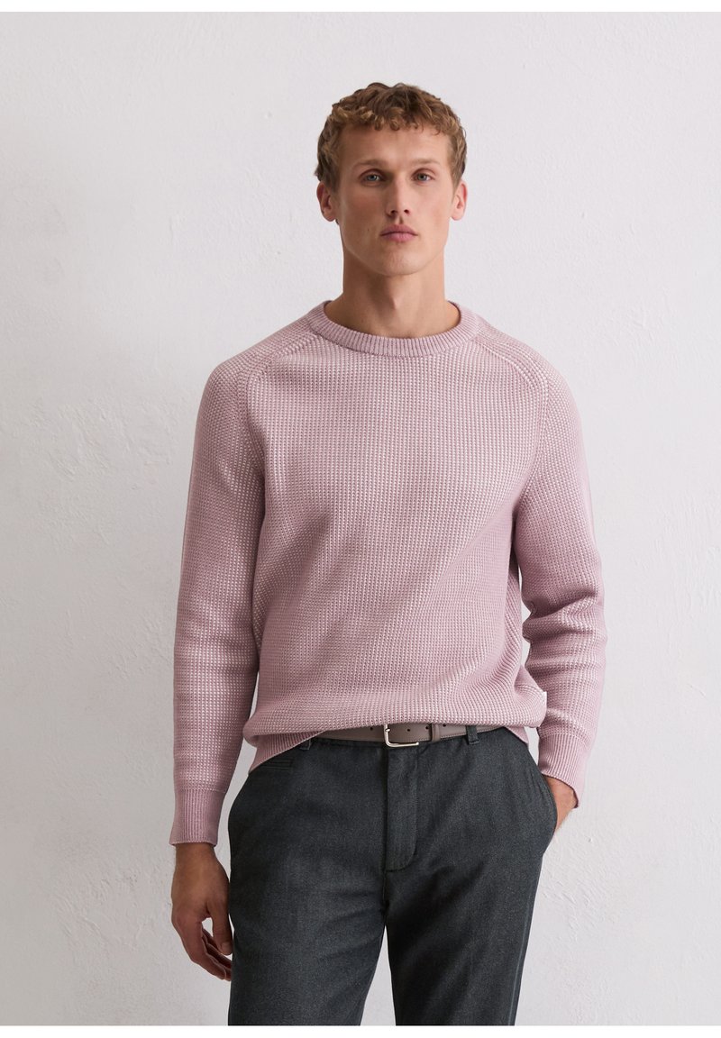Light pink knitted sweater with textured pattern, crew neckline, and long sleeves; paired with dark gray trousers featuring pockets.