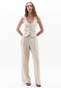 Beige linnen vest met knopen, gecombineerd met hooggetailleerde, wijde beige broeken. Soepele textuur, minimalistisch ontwerp, geen patronen of accenten.