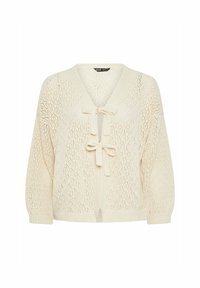 Stickad cardigan i krämfärg med V-hals, mönster av öppen arbetsmetod och snörning i midjan. Har långa, löst sittande ärmar.