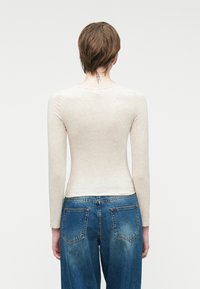 Top de manga larga color beige claro con corte ajustado, combinado con jeans de mezclilla de lavado medio que cuentan con bolsillos traseros y una textura ligeramente deslavada.