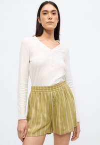 Ελαφρύ κρεμ χρώμα μακρυμάνικο τοπ με V-λαιμόκοψη και λεπτομέρεια με κουμπιά. Χακί ριγέ σορτς με ελαστική μέση και τρία κουμπιά.