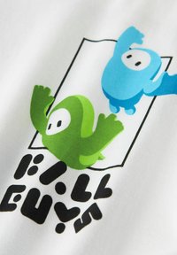 Camiseta de tela blanca con un gráfico de dos personajes coloridos: uno verde y otro azul, con el texto "Fall Guys" en letras negras y en negrita.