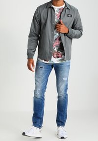 Šedá lehká bunda přes květinovou košili, v kombinaci s odřenými modrými džíny a bílými teniskami. Neformální, prodyšný outfit.
