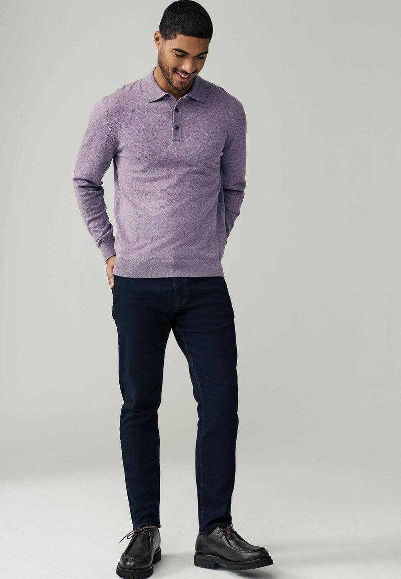 Paarse long-sleeve polo met een kraag en een drie-knopenlijst, gecombineerd met donkerblauwe slim-fit jeans en donkere schoenen.