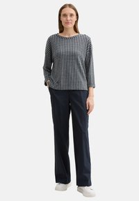 Pantaloni navy con una vestibilità morbida abbinati a un top a fantasia check bianco e nero. Il top presenta un collo rotondo e maniche lunghe.
